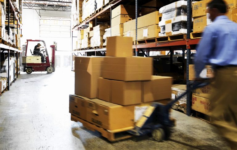 Employé manipulant des cartons à l'aide d'un transpalette dans un entrepôt.